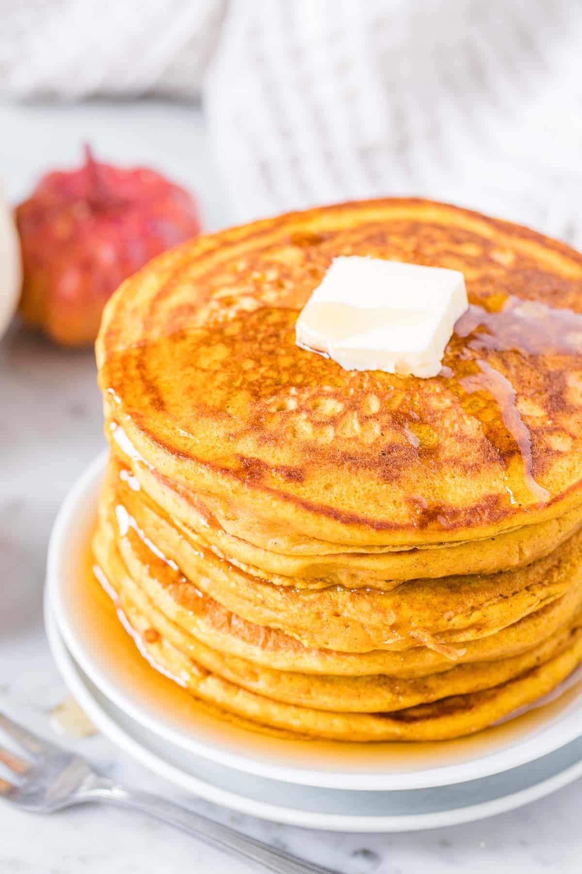 Une pile de crêpes à la citrouille garnies de beurre et de sirop d'érable.