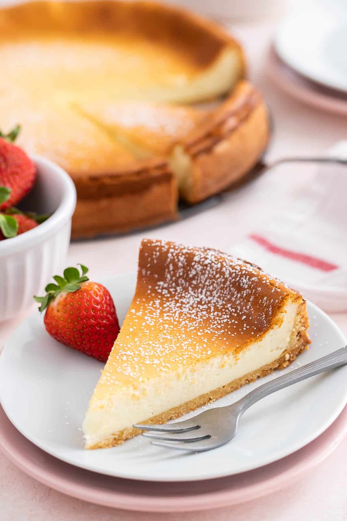 Une tranche de cheesecake sur une assiette blanche avec une fourchette à côté.