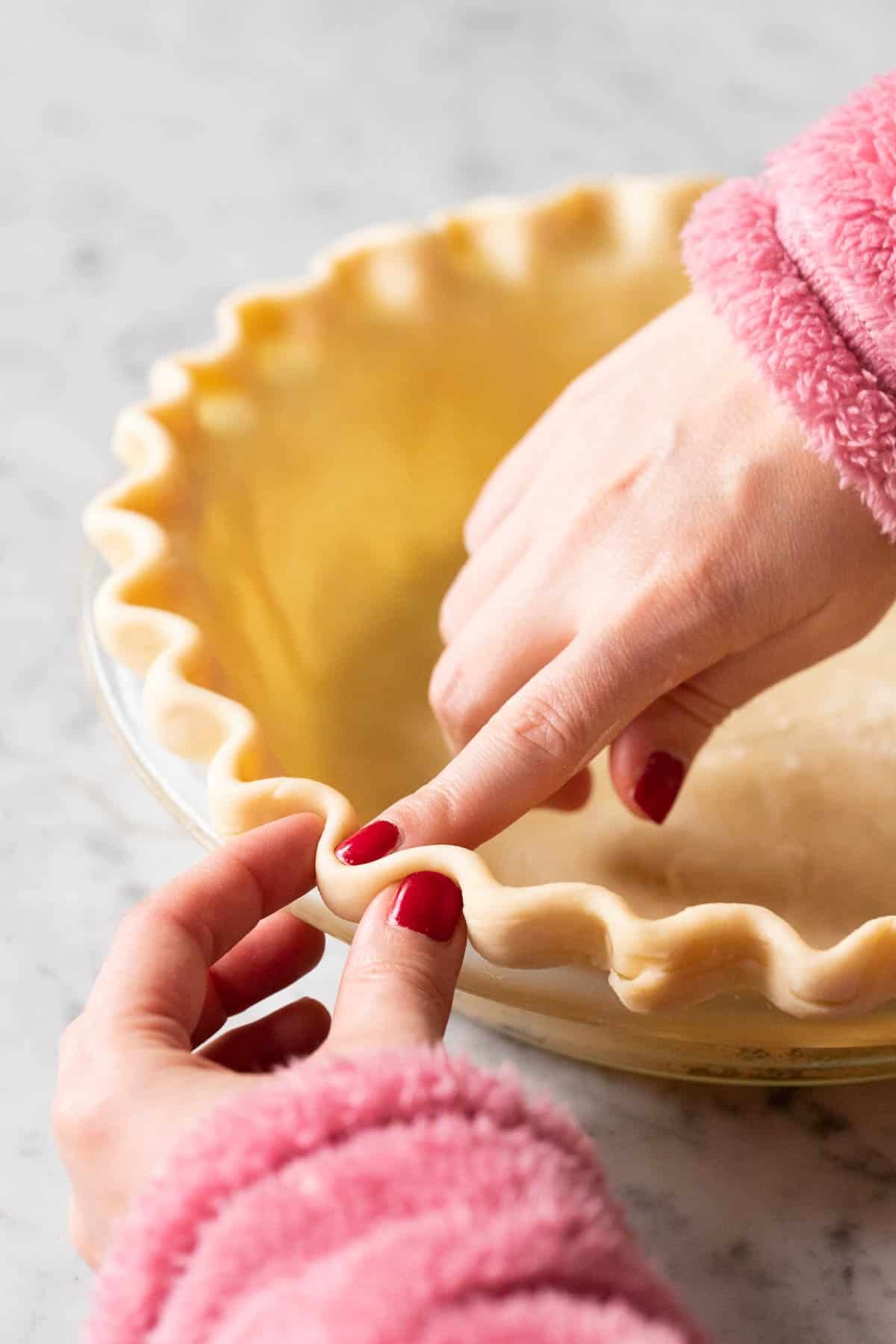 Deux mains façonnant une pâte à tarte cannelée.