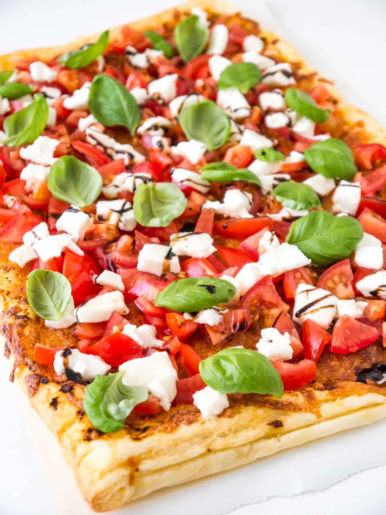 Pizza en pâte feuilletée tomate mozzarella avec tomates, mozzarella, feuilles de basilic et glaçage balsamique.
