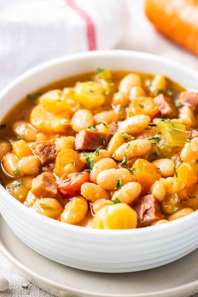 Un bol blanc contenant de la soupe de jambon et de haricots blancs, garni de persil.