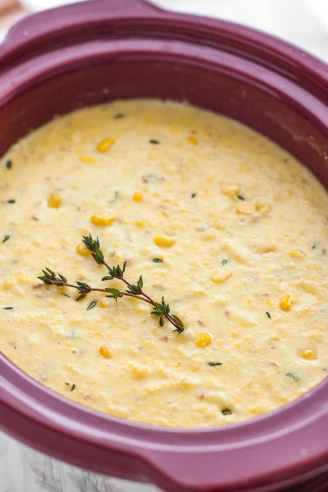 Un pot de mijoteuse rouge avec de la soupe de maïs et une branche de thym sur le dessus.