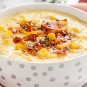 Gros plan d'un bol blanc avec des taches argentées de soupe de maïs garnie de morceaux de bacon et de thym.