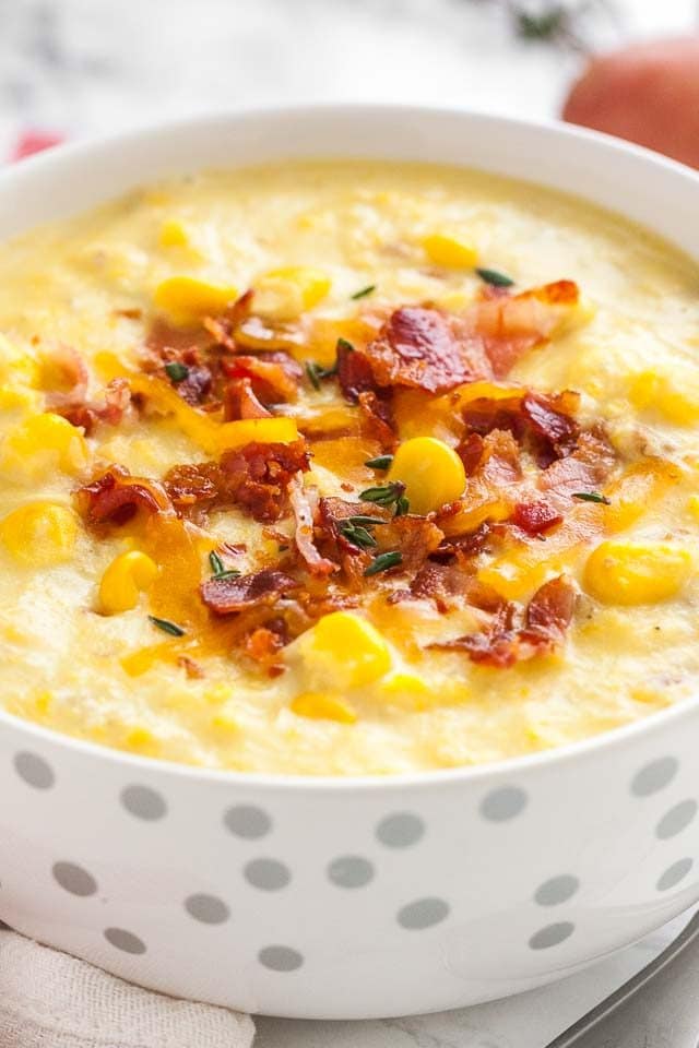 Gros plan d'un bol blanc avec des taches argentées de soupe de maïs garnie de morceaux de bacon et de thym.