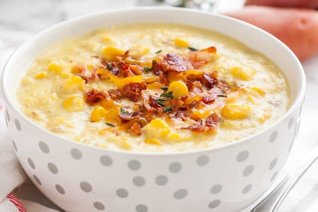 Gros plan d'un bol blanc avec des taches argentées de soupe de maïs garnie de morceaux de bacon et de thym.