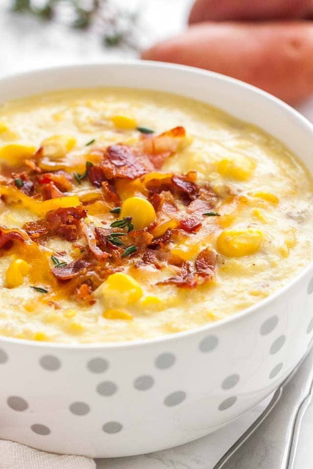 Gros plan d'un bol blanc avec des taches argentées de soupe de maïs garnie de morceaux de bacon et de thym.