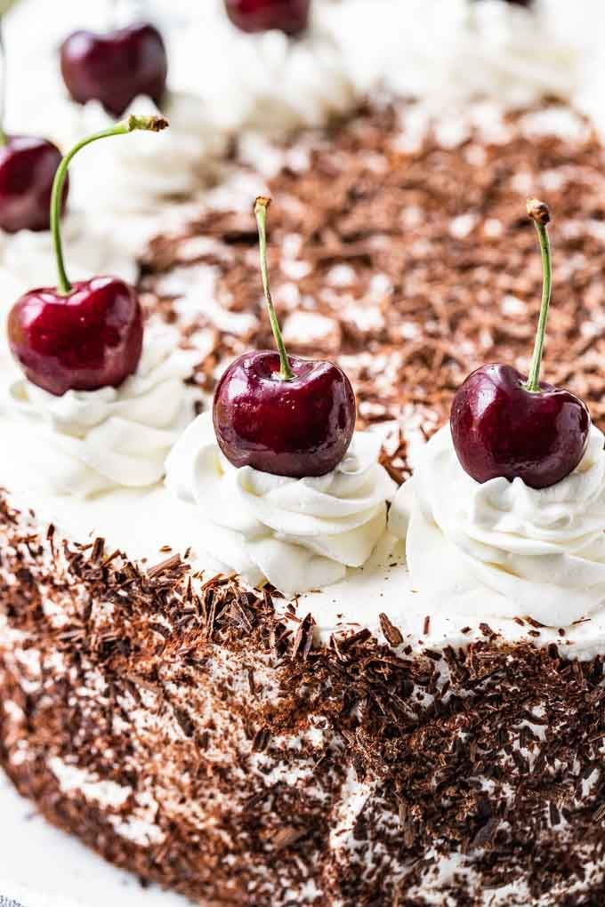 Gros plan sur un gâteau Forêt-Noire. Le gâteau a des copeaux de chocolat sur les côtés et des tourbillons de crème fouettée garnis de cerises entières au-dessus