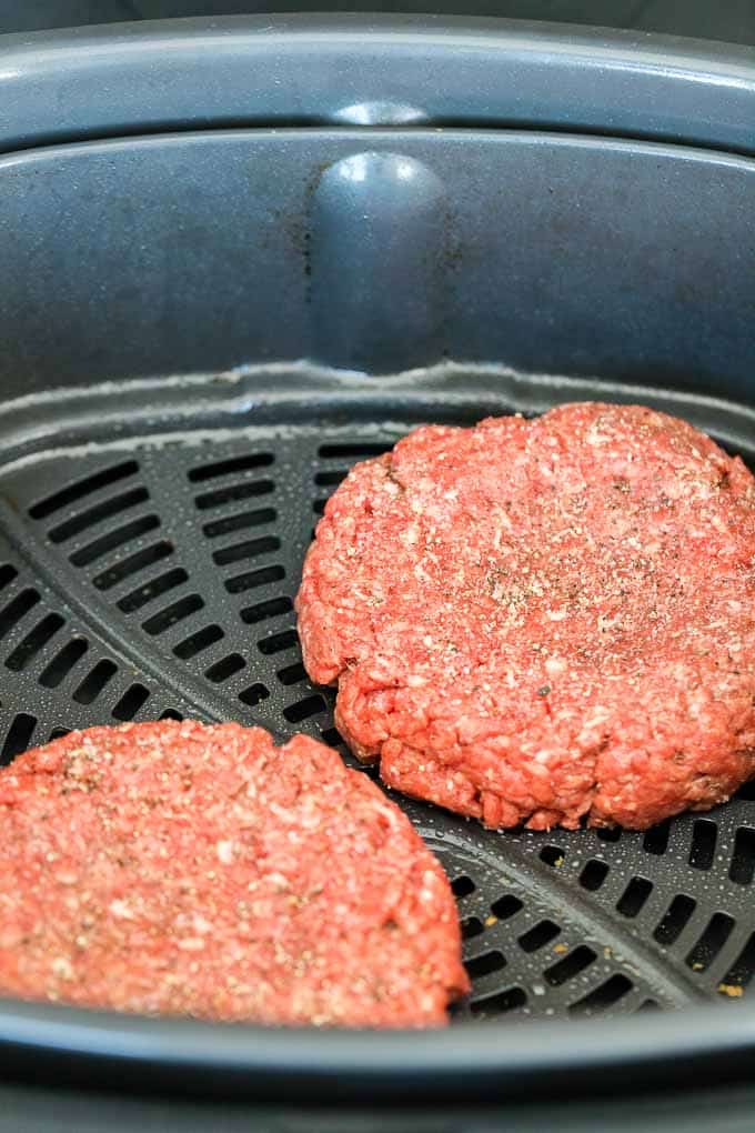 Deux galettes de hamburger crues dans le panier de la friteuse à air