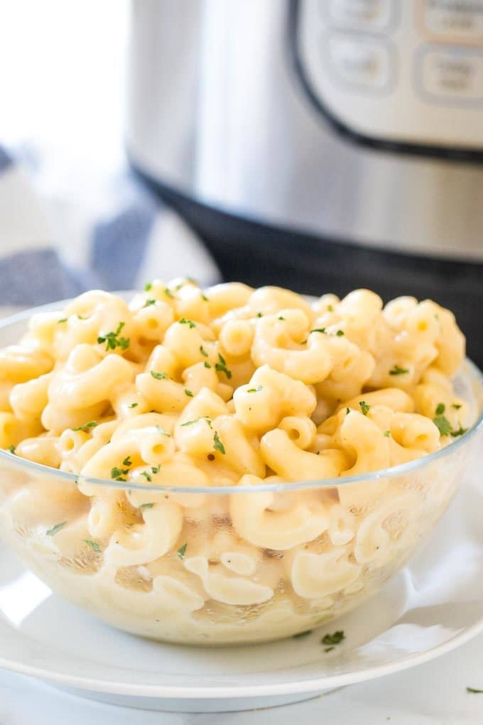 Mac and Cheese dans un bol en verre, garni de persil avec une mijoteuse en arrière-plan