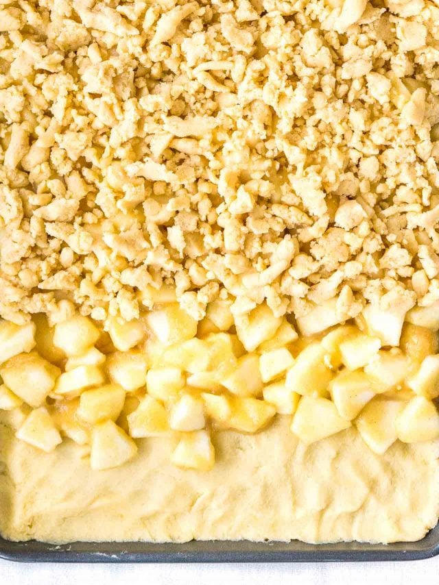 gâteau à la pomme streusel non cuit avec les couches partiellement finies pour montrer le processus : étaler la pâte sur la plaque, ajouter le mélange de pommes, garnir de streusel
