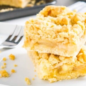 deux morceaux de gâteau streusel aux pommes empilés l'un sur l'autre sur du papier sulfurisé avec une fourchette à côté et une plaque de cuisson en arrière-plan