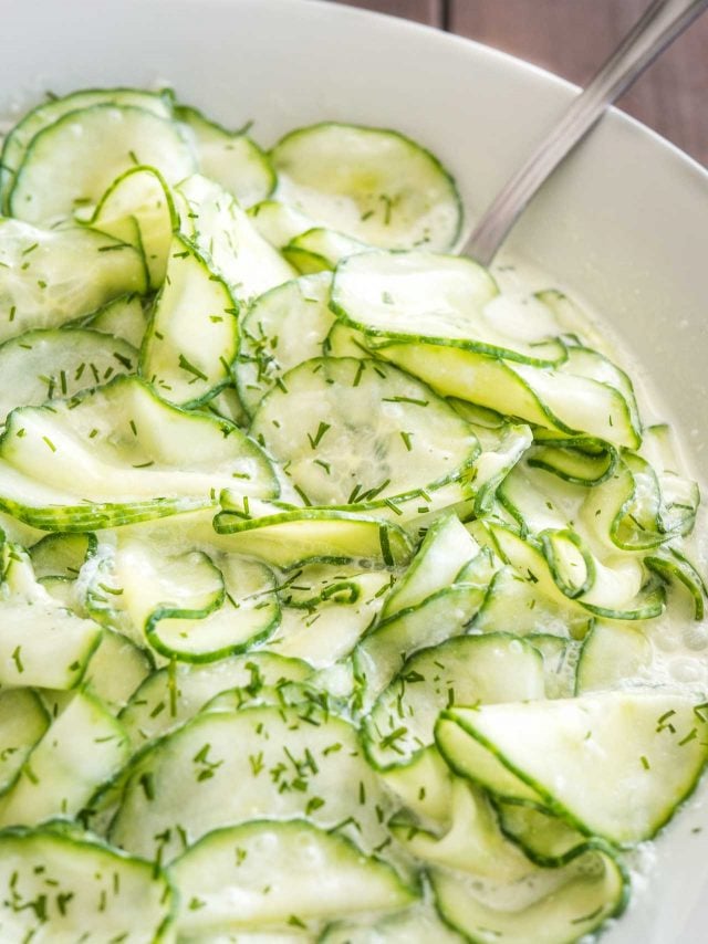 Gros plan de la salade de concombre allemande dans un bol de salade blanc avec une cuillère dedans