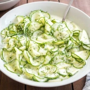 Salade de concombre allemande dans un bol de salade blanc sur une table en bois avec une cuillère dedans.
