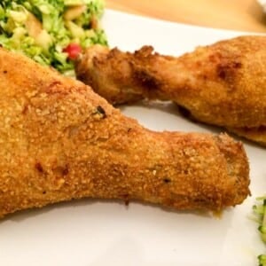 deux cuisses de poulet panées sur un papier sulfurisé avec une salade de courgette en arrière-plan