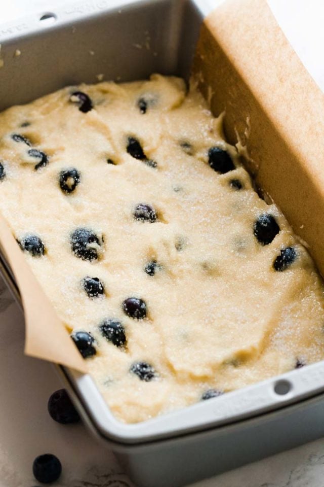 Un moule à gâteau, tapissé de papier sulfurisé, rempli de pâte avec des myrtilles.