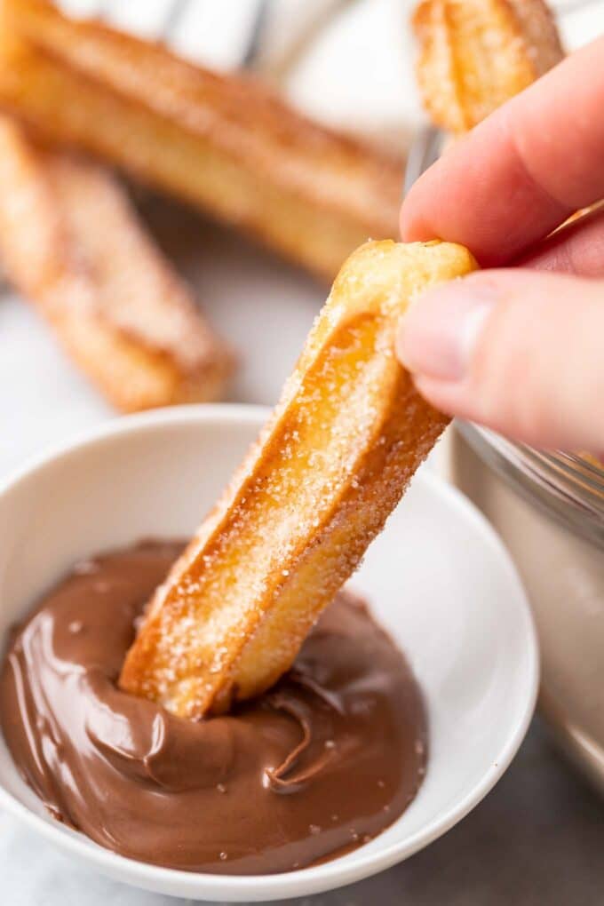 churro sucré trempé dans du nutella, avec des churros en arrière-plan