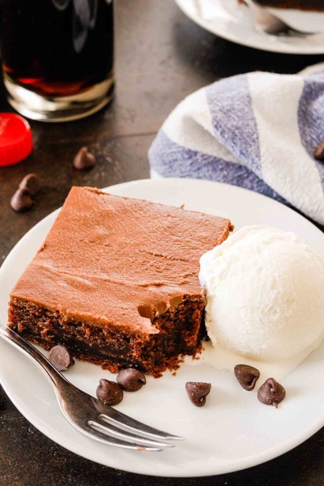 une tranche de gâteau au coca-cola sur une assiette blanche avec de la glace à la vanille, une fourchette, et des pépites de chocolat avec une bouchée enlevée
