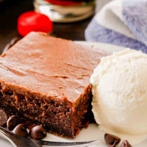 une tranche de gâteau au coca-cola sur une assiette blanche avec de la glace à la vanille, une fourchette et des pépites de chocolat avec un torchon blanc et bleu et un bouchon de bouteille de coca-cola en arrière-plan