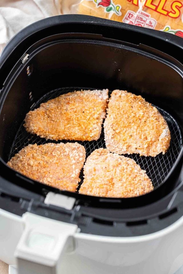 Quatre poitrines de poulet panées dans un panier de friteuse à air.