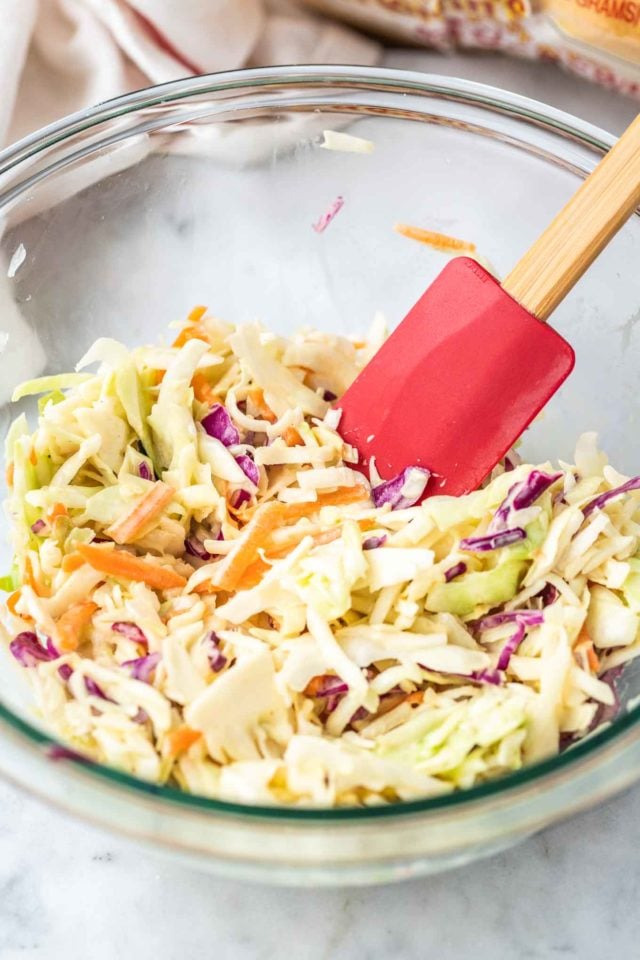 Un bol en verre de salade de chou avec une spatule rouge à manche en bois à l'intérieur.