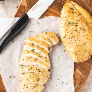 Deux poitrines de poulet frites sur une planche à découper en bois sombre et du papier sulfurisé avec un couteau en céramique à côté. Une poitrine de poulet est tranchée.