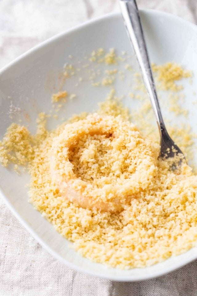 Une rondelle d'oignon dans des miettes de panko sur une assiette blanche avec une fourchette.