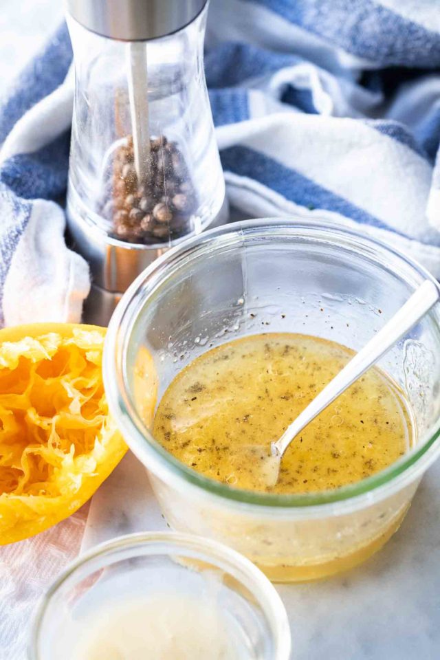 vinaigrette dans un bol en verre avec une cuillère à l'intérieur et une orange pressée et un moulin à poivre en arrière-plan