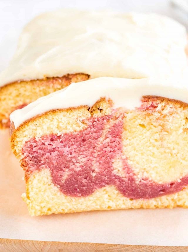 Gros plan d'un gâteau au yaourt aux framboises sur une planche à découper en bois recouverte de papier sulfurisé. Une tranche a été coupée et est appuyée contre.