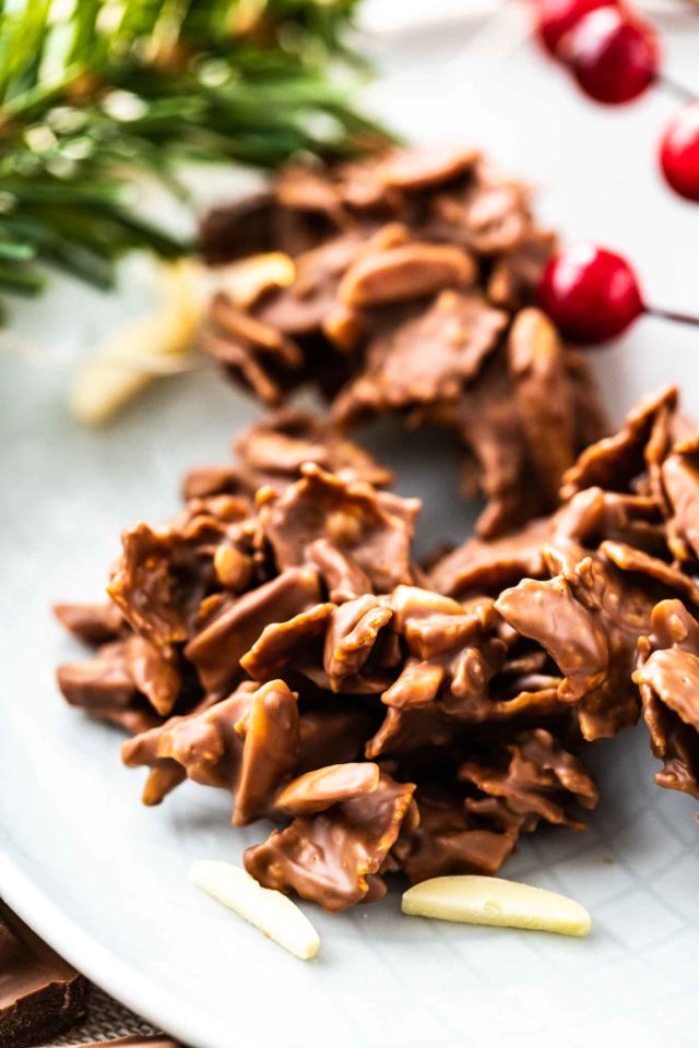 Gros plan sur des clusters de corn flakes et d'amandes enrobés de chocolat sur une assiette grise, garnis d'amandes et de cranberries