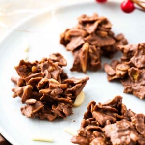 clusters de corn flakes et d'amandes enrobés de chocolat sur une assiette grise, garnis d'amandes et de cranberries