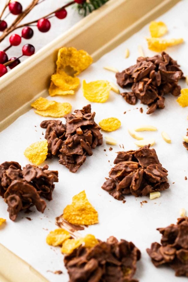 clusters de corn flakes et d'amandes enrobés de chocolat sur du papier sulfurisé dans un plat de cuisson, garnis de corn flakes, d'amandes et de cranberries