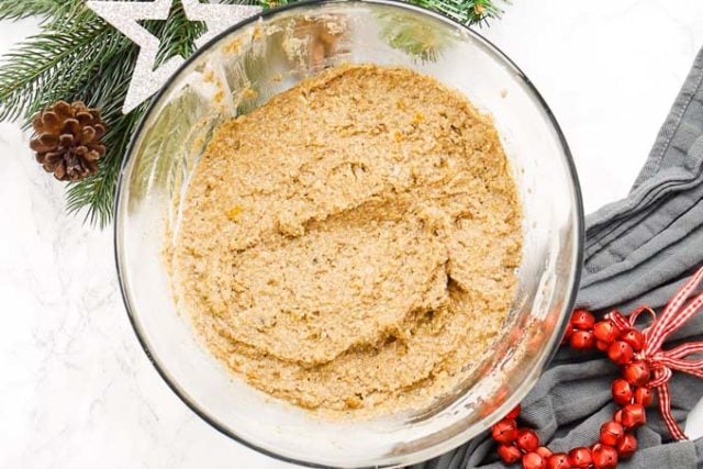 Un bol en verre avec de la pâte à lebkuchen à côté de quelques clochettes rouges et quelques branches de pin