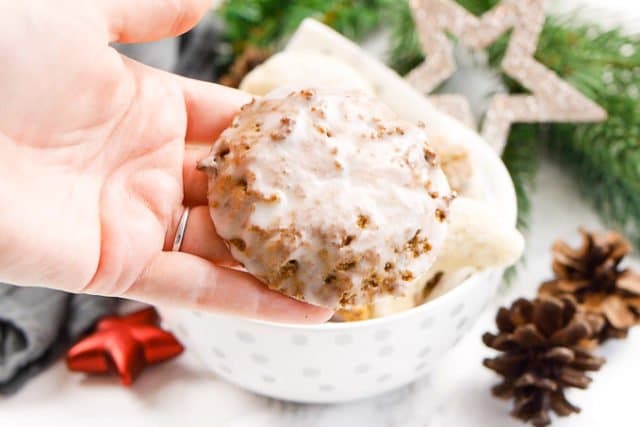Une main tenant un lebkuchen glacé au sucre. Il y a un bol blanc avec des biscuits de Noël en arrière-plan.