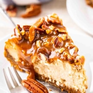 Une part de cheesecake garnie de noix de pécan et de sauce caramel sur une petite assiette blanche avec une fourchette.