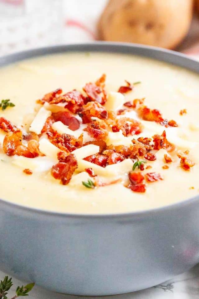 Gros plan d'un bol gris de soupe de pommes de terre garni de miettes de bacon, de bandes de fromage et de thym.