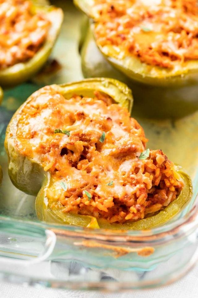Gros plan sur un plat de cuisson en verre avec des poivrons verts farcis cuits garnis de persil.