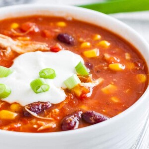 Gros plan d'un bol blanc de chili au poulet, garni de crème aigre et de ciboulette.