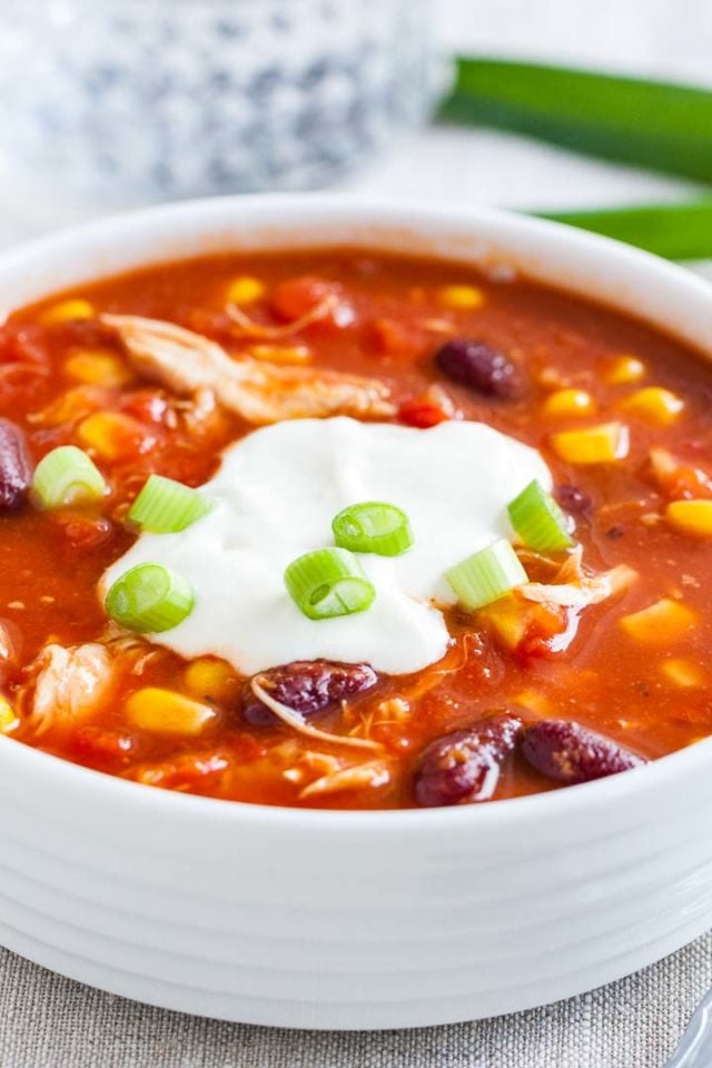 Gros plan d'un bol blanc de chili au poulet, garni de crème aigre et de ciboulette.