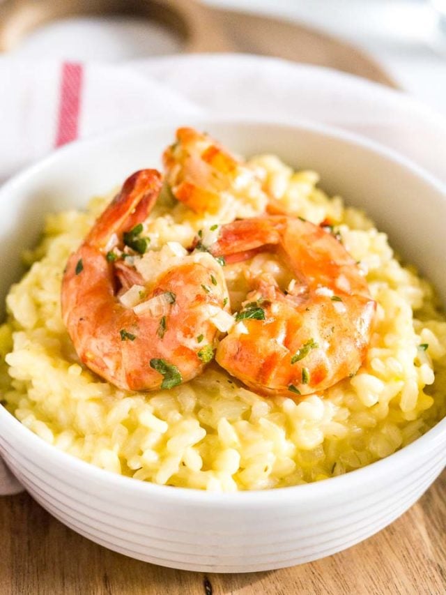 Gros plan d'un bol blanc avec du risotto au safran et des crevettes frites sur un torchon de cuisine blanc avec une rayure rouge.