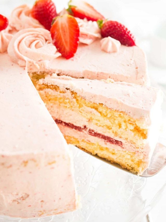 Gros plan d'un gâteau aux fraises, garni de fraises, avec une part étant soulevée par une spatule à gâteau.