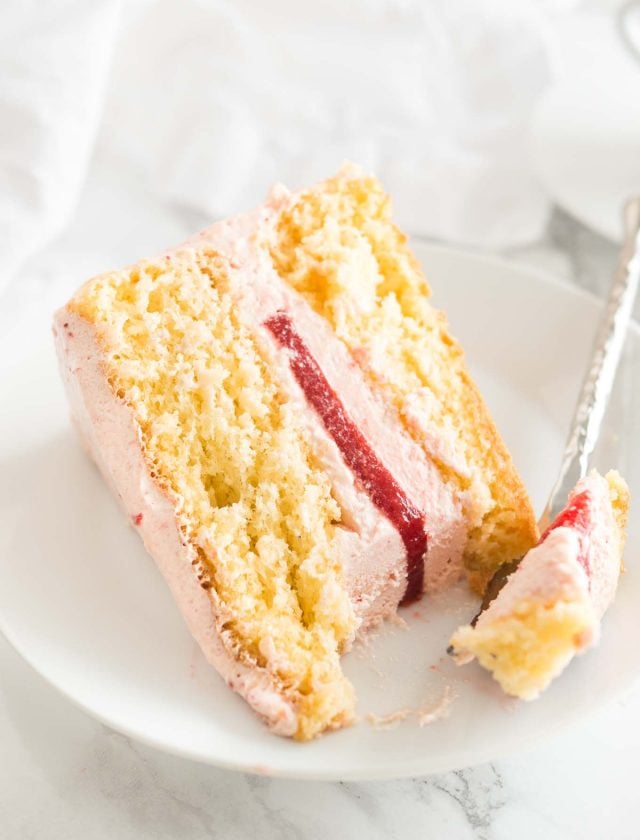 Une part de gâteau aux fraises sur une assiette blanche. Une fourchette prend un morceau de la part.