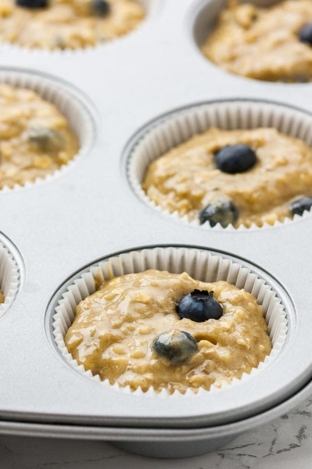 Un moule à muffins garni de caissettes en papier remplies de pâte et de myrtilles.