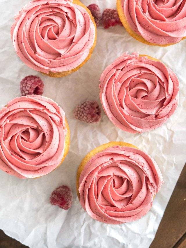 Vue de dessus de cupcakes au citron et framboise avec glaçage framboise rose à côté de quelques framboises sur du papier sulfurisé.