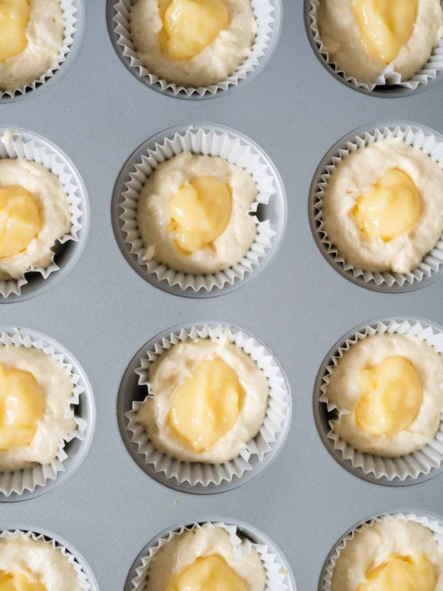 Vue de dessus d'un moule à muffins, garni de caissettes à muffins, rempli de pâte et de cuillerées de lemon curd.