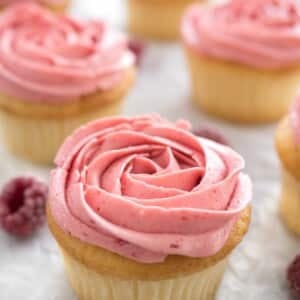 Cupcakes au citron et framboise avec glaçage framboise rose à côté de quelques framboises.