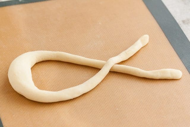 Pâte à bretzel, après avoir été façonnée en forme de saucisse, étalée en forme de ruban sur un tapis de cuisson en silicone.