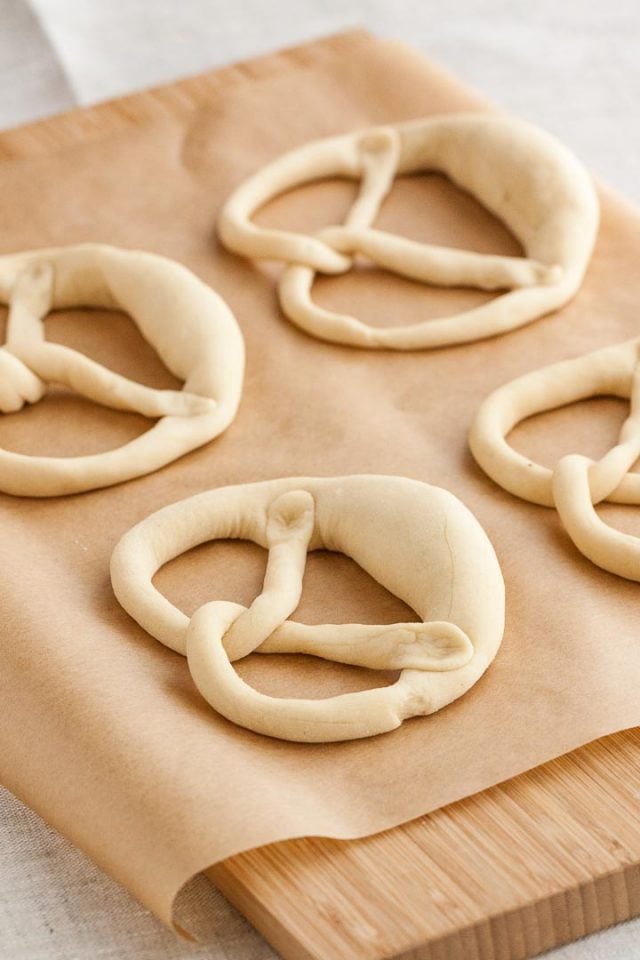 Quatre bretzels sur du papier sulfurisé avant la cuisson.