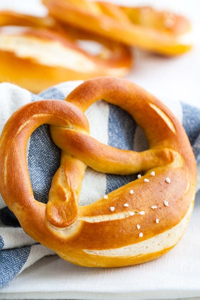 Gros plan d'un bretzel appuyé contre une serviette blanche et bleue pliée, avec d'autres bretzels en arrière-plan.
