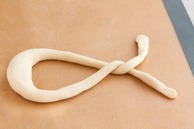 Pâte à bretzel étalée en ruban et tordue autour du point de contact une fois sur un tapis de cuisson en silicone.