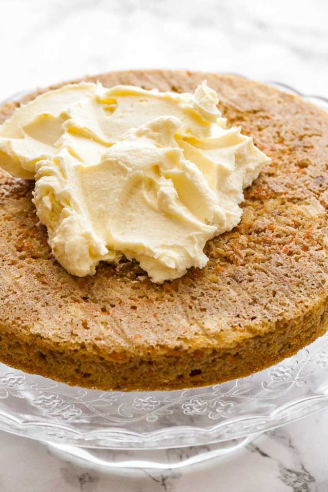 La couche inférieure d'un gâteau aux carottes et ananas sur un plateau de service en verre avec une touche de glaçage au cream cheese.